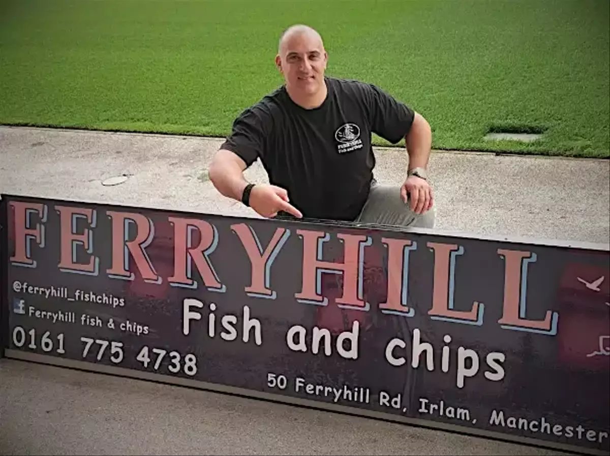 ferryhill owner Christos kneeling beside a pitchside ad board for his business